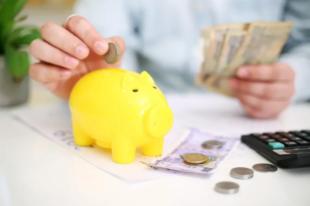 Kalkulator, monety i pióro na biurku, symbolizujące planowanie finansów i obliczanie raty kredytu hipotecznego.